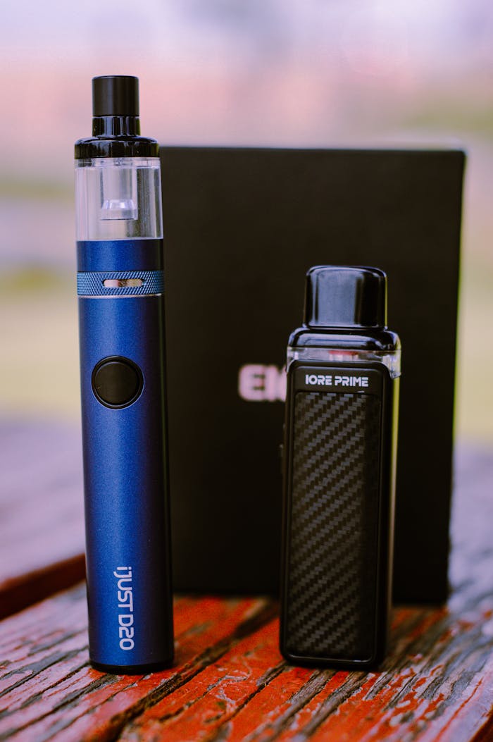 Detailed shot of blue and black vape devices on a wooden table, showcasing design and portability.