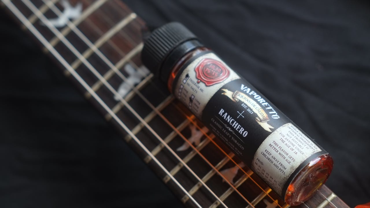 A close-up image showing a vaping liquid bottle resting on a guitar, highlighting music and vaping themes.